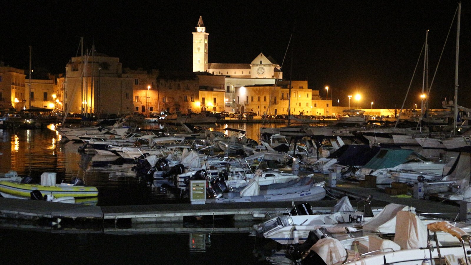 Il porto medievale di Trani al tramonto, con le barche ormeggiate e il campanile della cattedrale sullo sfondo